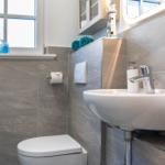 Badezimmer mit Waschbecken, Toilette und Fenster. Auf dem Waschtisch liegen Handtücher.