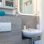 Badezimmer mit Waschbecken, Spiegel und Handtuch. Wandverkleidung grau, Tür weiß.