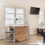 Essbereich mit Tisch, Stühlen und TV an der Wand. Fenster und Holzboden.