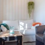 Ein Wohnzimmer mit Sofa, Sessel, Tisch und Pflanzen. Wand mit Streifenmuster.