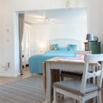 Ein Raum mit Tisch und Stühlen. Durchgehendes Fenster und Blick in Schlafzimmer mit Bett.