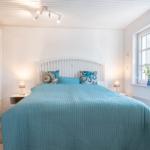 Schlafzimmer mit Bett, Nachttischen und Fenster. Decke weiß, Bett mit blauer Bettdecke.