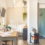 Wohnbereich mit Sofa, Esstisch, Fernseher und Kaminofen. Wand mit Streifen und hängende Pflanze.