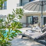 Pool area with lounge chairs and umbrellas. Modern house in the background.