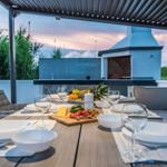 Terrace with set table, grill, and seating. Background with plants and sky.