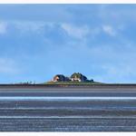 Haus auf Hügel über Wattlandschaft mit blauem Himmel