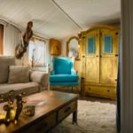 Ein Wohnzimmer mit Sofa, blauem Stuhl und Holzschrank. Auf dem Tisch stehen dekorative Objekte.