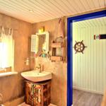 Badezimmer mit Waschbecken auf Holzschrank, Spiegel und Tür zum Duschbereich mit Ruder.