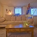 Ein Wohnzimmer mit Sofa, Couchtisch und Fenstern. An der Wand hängt eine Meerjungfrau.