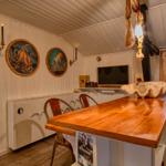 Küche mit Holztisch, Wandbildern und TV. Fenster mit Vorhang.