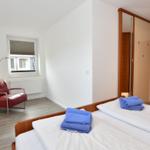 Schlafzimmer mit Bett, rotem Sessel und Kleiderschrank.