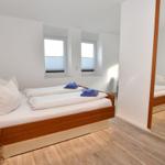 Schlafzimmer mit Doppelbett, zwei Fenstern und Spiegeltüren.