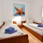 Zwei Einzelbetten mit weißen Laken und blauen Handtüchern. Wandbild mit Seestern.