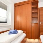 Zimmer mit zwei Betten, Holzschrank und Fenster mit Jalousie.