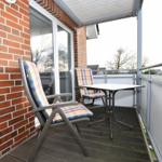 Terrasse mit Tisch und zwei Stühlen, Wand aus roten Ziegeln, Blick auf Bäume.