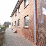 Rotes Backsteinhaus mit Fenstern und Hausnummer 80. Pflasterweg und Gartenbereich.