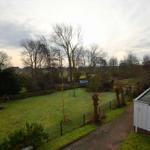 Grüner Garten mit Zaun, Bäumen und Terrasse. Blick auf einen Pool und einen Holzschuppen.