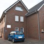 Zweistöckiges Haus mit rotem Ziegelmauerwerk und blauem Auto vor dem Eingang.