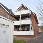 Zweistöckiges Haus mit Balkon und rotem Ziegelmauerwerk. Vor dem Haus steht ein weißer Container.