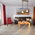 Wohnzimmer mit braunem Sofa, rotem Sessel und Holztisch. Große Glastür führt auf Balkon.