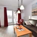 Wohnzimmer mit Sofa, Couchtisch und Balkon. Rote Vorhänge und Wandbild.