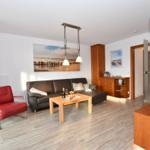 Wohnzimmer mit braunem Sofa, rotem Sessel und Holztisch. An der Wand hängt ein Bild.