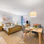 Schlafzimmer mit Bett, Tisch und Sofa. An der Wand hängt ein Bild.