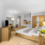 Schlafzimmer mit Holzbett, TV-Schrank und Blick in Küche und Essbereich.