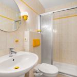 Badezimmer mit Dusche, Waschbecken und Toilette. Gelbe Akzente an den Wänden.