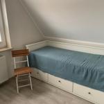 Ein Schlafzimmer mit Dachschrägen, weißem Bett und Holzstuhl neben dem Fenster.
