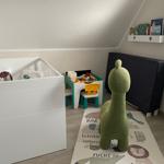 Kinderzimmer mit Babybett, Spielzeugtisch und grünem Stofftier auf Tiermuster-Teppich.