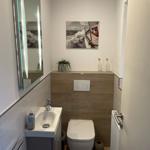 Badezimmer mit Waschbecken, Toilette und Spiegel. Wandbild zeigt Segelyacht.