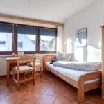 Zimmer mit zwei Betten, Schreibtisch, Kleiderschrank und Fenster mit Blick nach draußen.