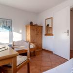 Zimmer mit zwei Betten, Holzmöbeln und Terrakottaboden. An der Wand hängt ein Bild eines Schiffs.