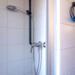 Dusche mit Handbrause und blauem Haartrockner an der Wand.