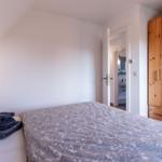 Schlafzimmer mit Bett, Holzschrank und Blick in das Badezimmer.