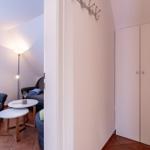 Wohnbereich mit Sitzgelegenheit, Tischen und Gardinen. Flur mit Kleiderständer und Schrank.