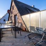 Terrasse mit Tisch, Stühlen und Liegen. Hintergrund: Backsteinhaus mit Dach und Satellitenschüssel.
