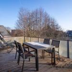 Terrasse mit Tisch, Stühlen und Liegestühlen. Blick auf Bäume und Häuser.