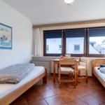 Zimmer mit zwei Betten, Tisch, Stühlen und Fenster mit Blick auf Gebäude.