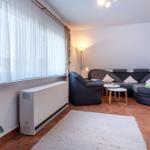 Wohnzimmer mit Sofa, Sessel, Tisch und Heizung an Fenster