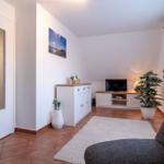 Wohnraum mit TV, Pflanzen und Tür. Terrakottaboden und weißer Schrank.