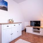 Wohnzimmer mit TV, Schrank und Pflanze. Wandbild zeigt Strand.