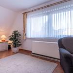 Wohnzimmer mit Sessel, Fernseher, Pflanze und Fenster mit Vorhängen.