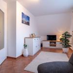 Wohnzimmer mit TV, Pflanzen und Tür zum Schlafzimmer. Terrakottafußboden und weiß lackierte Möbel.