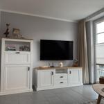 Wohnzimmer mit Fernseher, weißen Schränken und großem Fenster.
