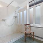 Dusche mit Glaswand, Holzstuhl und Fenster mit Milchglas