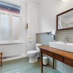 Badezimmer mit Waschtisch auf Holzbank, Toilette und Fenster mit Milchglas.
