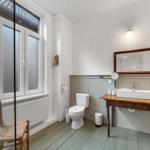 Badezimmer mit Toilette, Waschtisch und Fenster. Holzfußboden und rustikale Möbel.