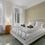 Schlafzimmer mit weißem Bett, zwei Nachttischen und großen Fenstern.